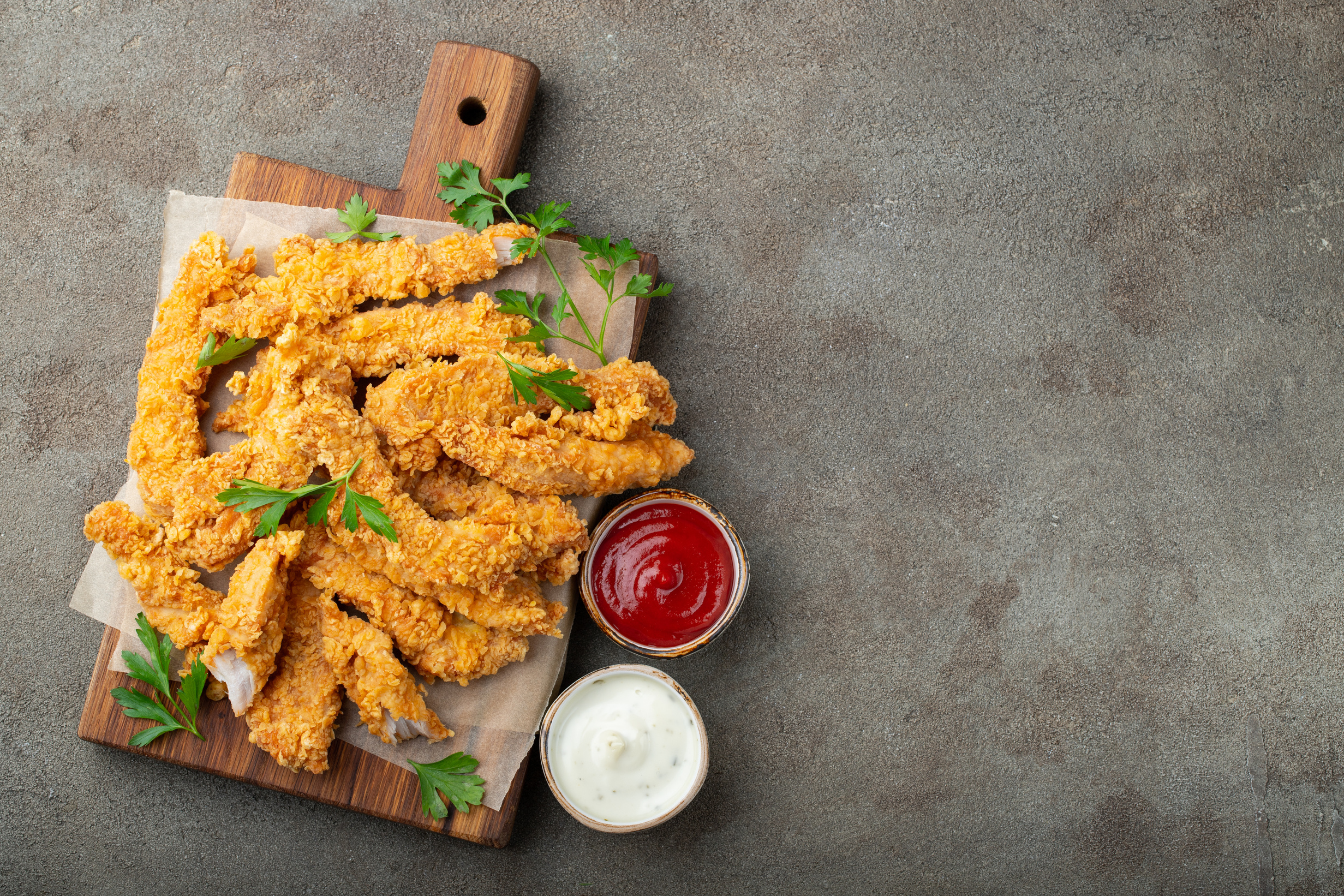 Breaded chicken strips with two kinds of sauces on a wooden Board. Fast food on dark brown background. Top view with copy space