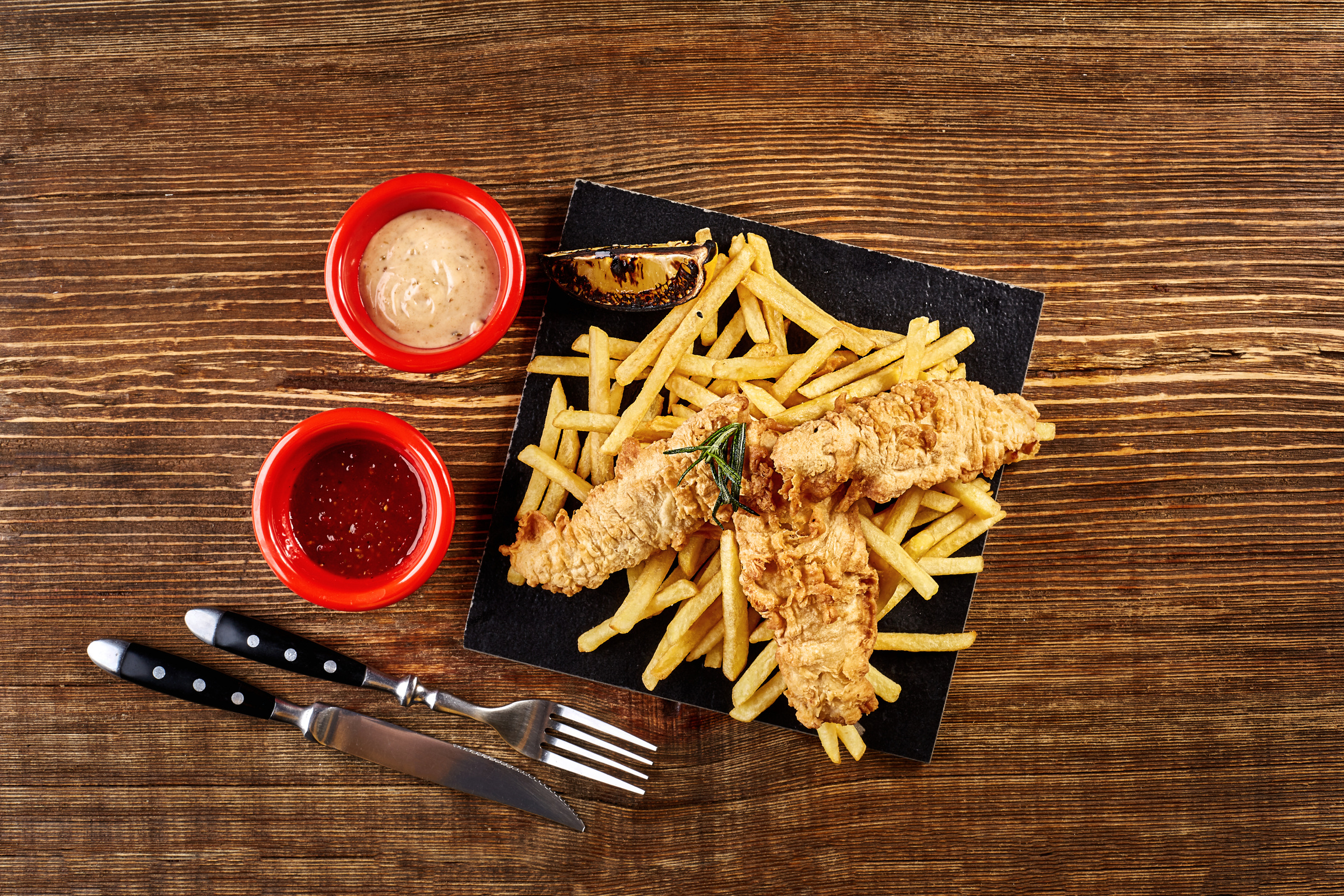 Black Plate with Fish and Chips, Mayo and Ketchup on Wooden Background